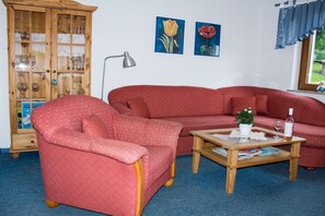 A living room with a red sofa, a matching armchair, a wooden coffee table, and a cabinet with glass doors. - Holiday apartment in Rhön with 1 bedroom (Hilders)