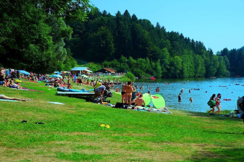 A lakeside setting with people relaxing on the grass, tents, and boats.