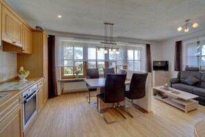 A modern kitchen with wooden cabinets, a dining area with a table and chairs, and a living room with a sofa and a TV. - Holiday apartment with 1 bedroom (Wegscheid)