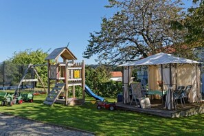A playground with a slide and climbing structure, a covered seating area with chairs, and a lawn. - Holiday apartment with 1 bedroom (Wegscheid)