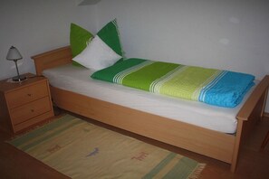 Un lit simple avec un cadre en bois, une table de chevet avec une lampe et un tapis à motifs.