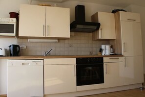 A kitchen with white cabinets, a black oven, a coffee maker, and a dishwasher. - Holiday apartment with 3 bedrooms (Fürsteneck)