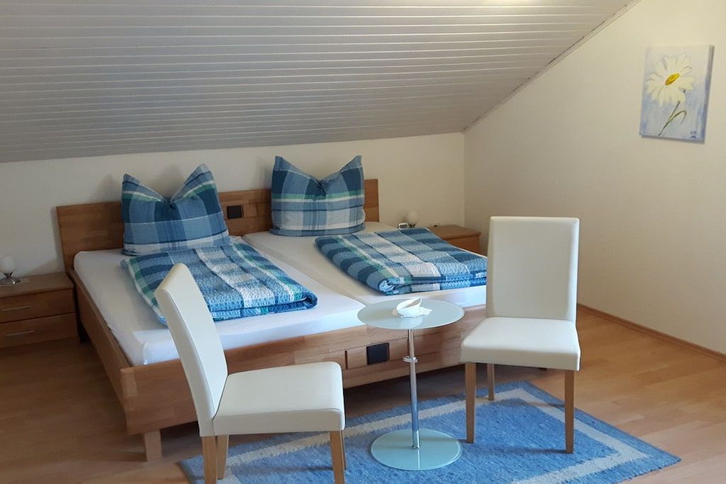 A bedroom with a bed, two pillows, a bedside table, a chair, and a small round table.