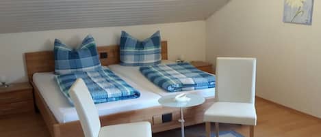 Een slaapkamer met een bed, twee kussens, een nachtkastje, een stoel en een klein rond tafeltje.