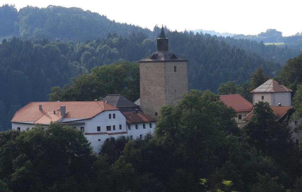 Un edificio histórico con una torre destacada, rodeado de abundante vegetación y colinas.