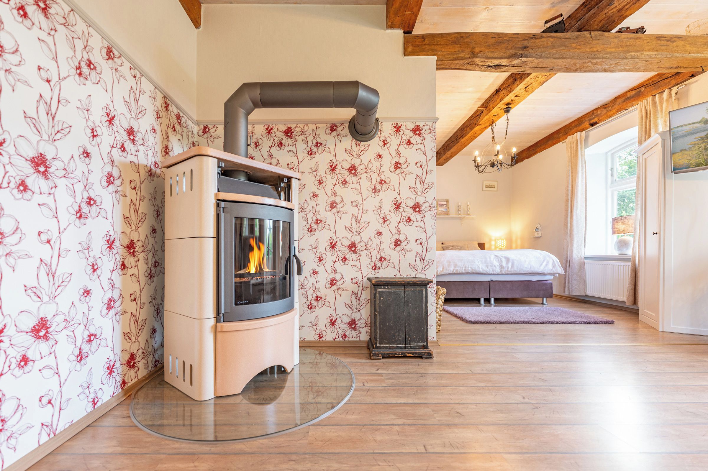 A room with a wood-burning stove, a bed, and a window with curtains.