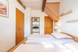 A bedroom with a bed, a wooden wardrobe, a shelf with books, and a small table with a lamp.