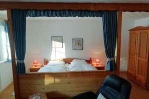 A bedroom with a wooden bed, two bedside lamps, a wardrobe, and a window with curtains. - Holiday apartment with 2 bedrooms (Oberreute.)