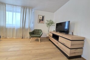 Un soggiorno con una poltrona verde, un televisore a schermo piatto su un mobile in legno e una pianta in vaso.