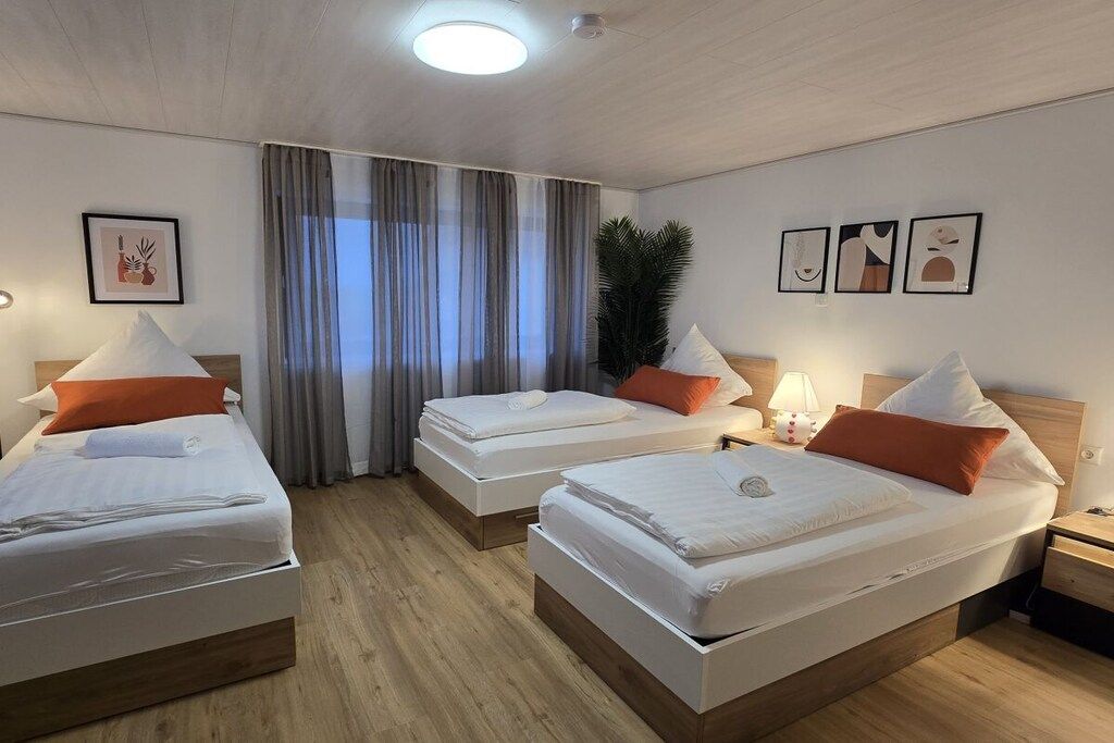 Une chambre d’hôtel avec trois lits, une grande fenêtre avec des rideaux et des œuvres d’art accrochées aux murs.