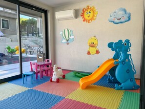 Un espace de jeux pour enfants avec un toboggan, des tapis colorés et des décorations murales ludiques.