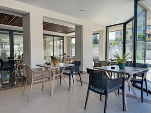 Un espace de restauration intérieur avec des tables et des chaises, de grandes fenêtres et une vue sur l’extérieur.