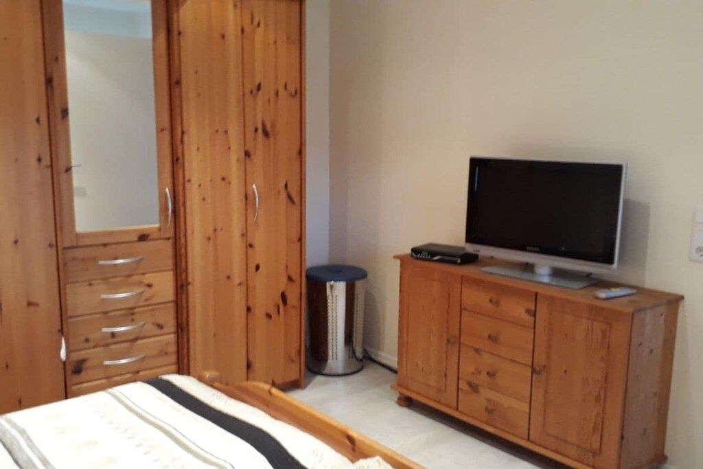 Un dormitorio con cama, un armario de madera, un televisor sobre un mueble bajo y un cubo de basura.