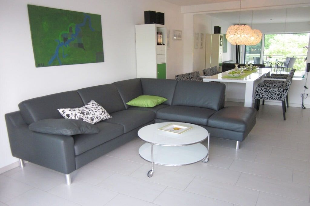 Een moderne woonkamer met een grijze modulaire bank, een ronde salontafel en een eethoek met gestreept beklede stoelen.