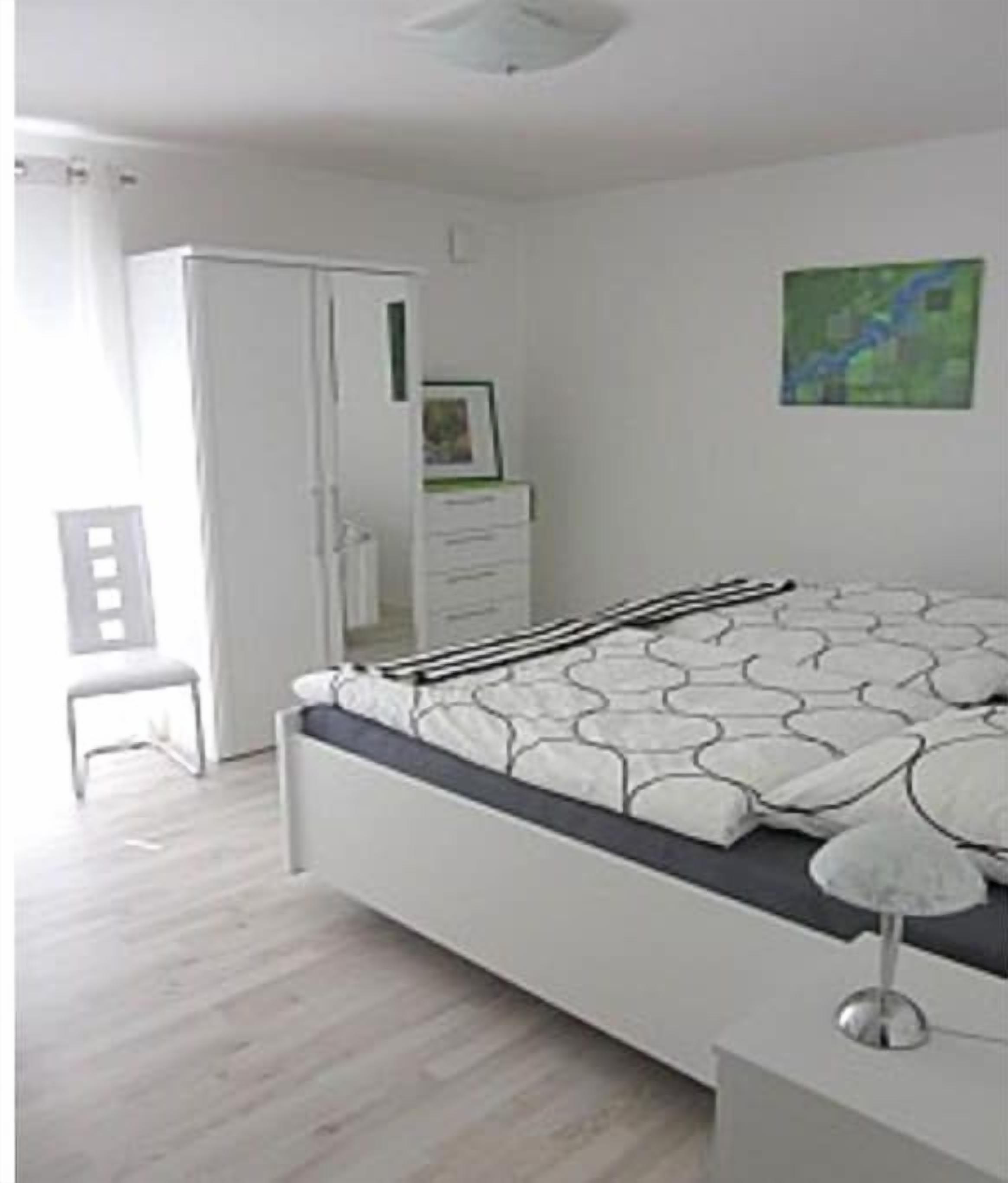 Un dormitorio con cama, mesita de noche, silla, armario y un cuadro en la pared.