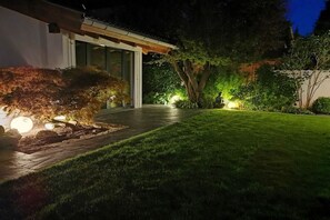 Un espace jardin bien éclairé, avec un chemin menant à un bâtiment moderne doté de grandes fenêtres.