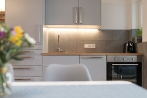 Une cuisine moderne avec des meubles gris, un plan de travail en bois, un four encastré et une petite plante posée sur le plan de travail.