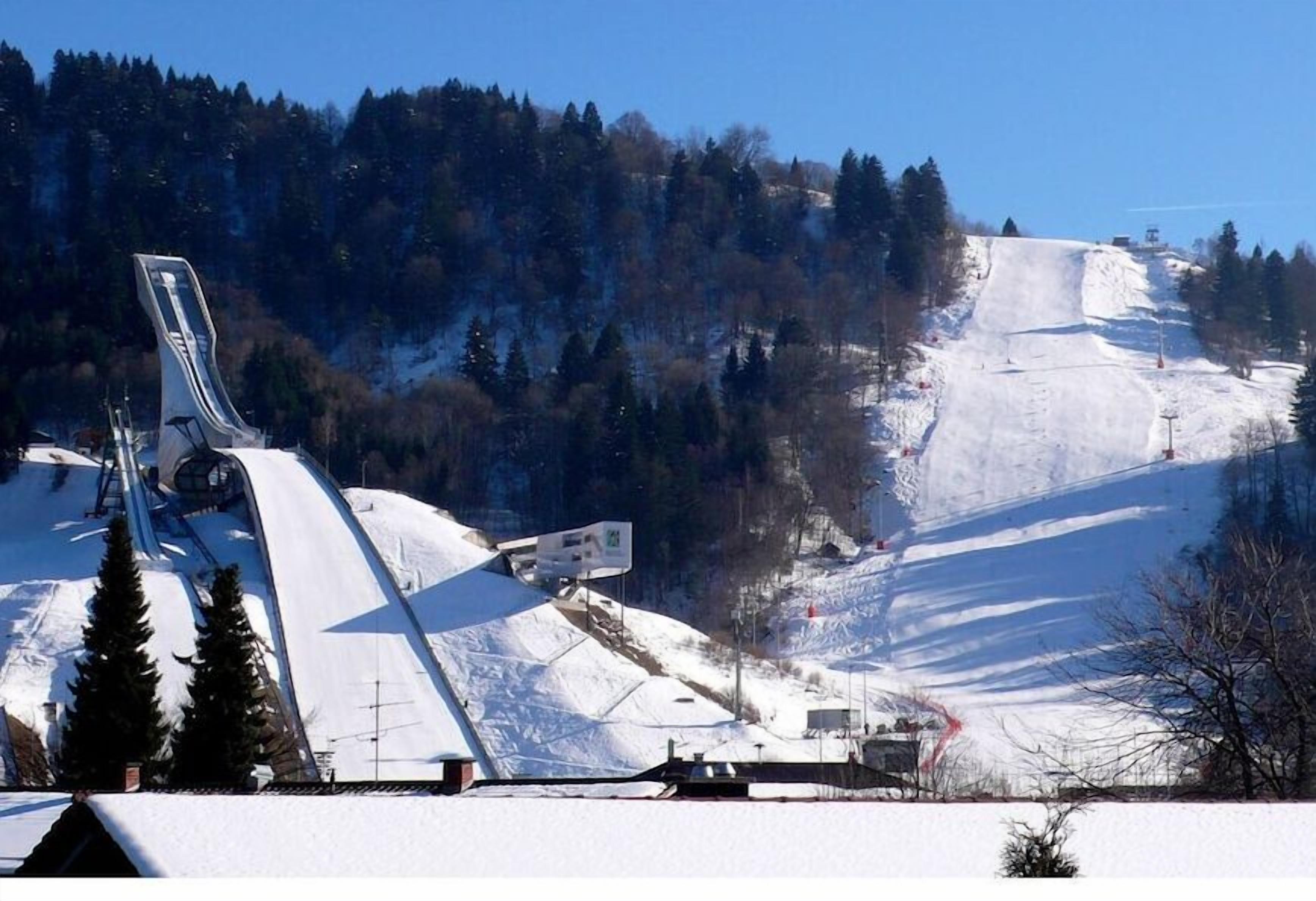 A snow-covered ski slope with a chairlift and trees in the background.