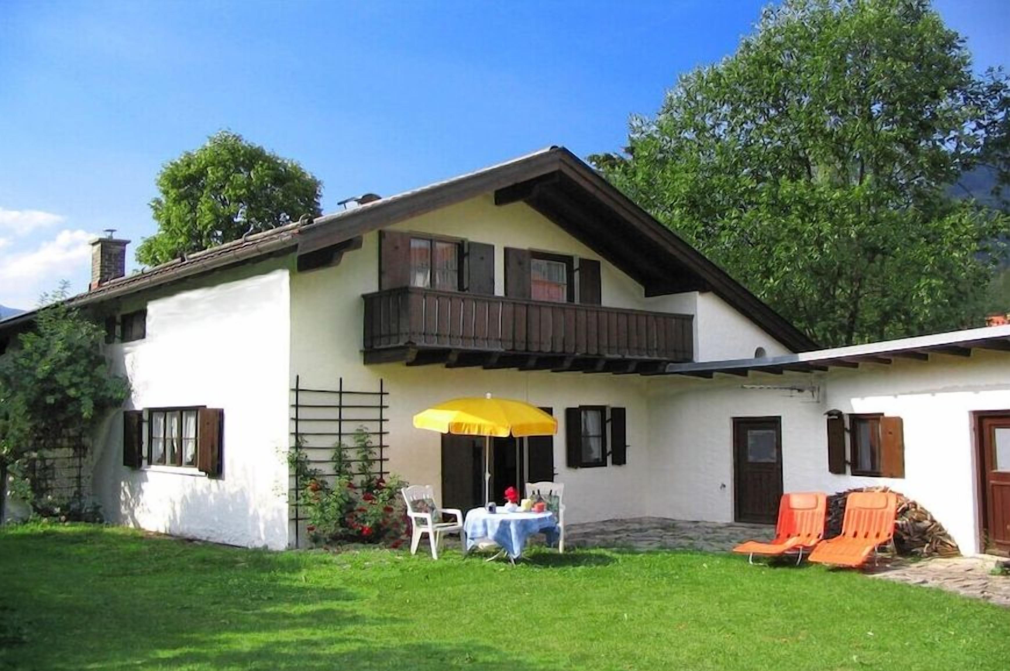 Une maison à deux étages avec un balcon, une table avec des chaises et un parasol jaune.