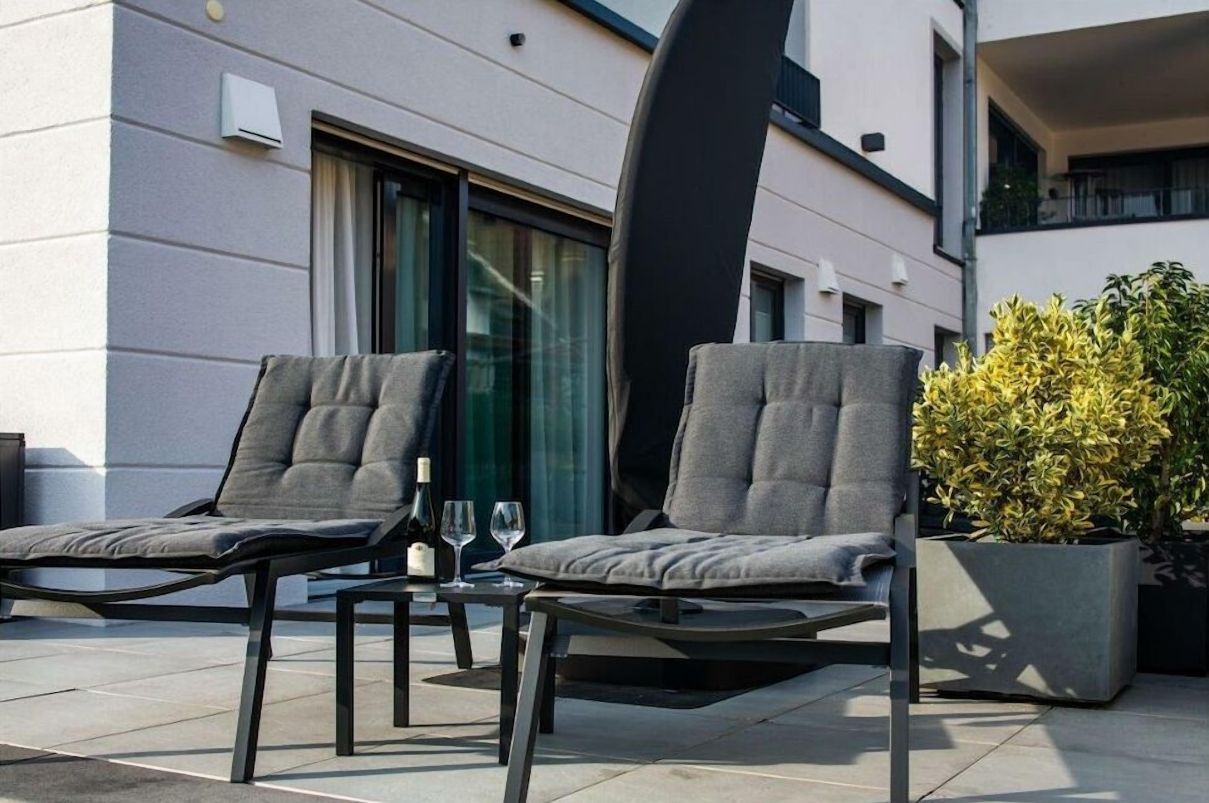 Two lounge chairs with cushions, a table with a bottle and glasses, and a potted plant.