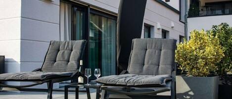 Two lounge chairs with cushions, a table with a bottle and glasses, and a potted plant.