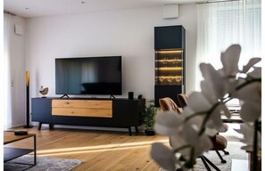 Un saló modern amb un televisor de pantalla plana, un moble de televisió negre amb vidrieria, un paviment de fusta i una planta en test.