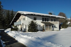 A two-story house with a snow-covered roof and a driveway leading to the entrance. - Holiday apartment with 1 bedroom (Bischofswiesen)