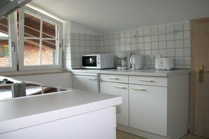 A kitchen with white cabinets, a microwave, a coffee maker, and a window with a view of a brick wall. - Holiday apartment with 1 bedroom (Bischofswiesen)
