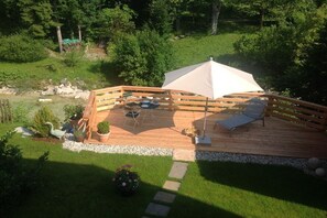 Un terrazzo in legno con mobili da esterno, un ombrellone e uno stagno.