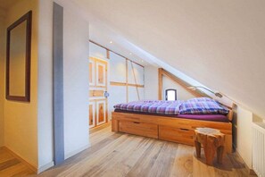 A bedroom with a sloped ceiling, a bed with a plaid bedspread, wooden flooring, and a small wooden stool. - Holiday apartment with 1 bedroom (Ehrenberg)
