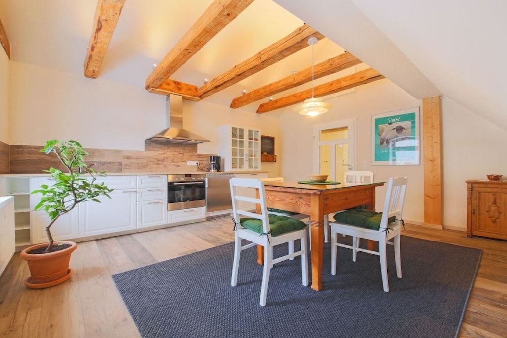 Una cucina con travi in legno, mobili bianchi, un tavolo da pranzo con sedie e una pianta in vaso.