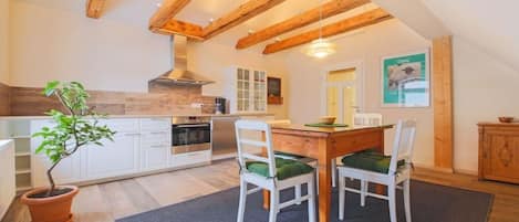 A kitchen with wooden beams, white cabinets, a dining table with chairs, and a potted plant.