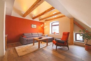A cozy living room with a sloped ceiling, a sofa, a chair, a small table, and a potted plant. - Holiday apartment with 1 bedroom (Ehrenberg)
