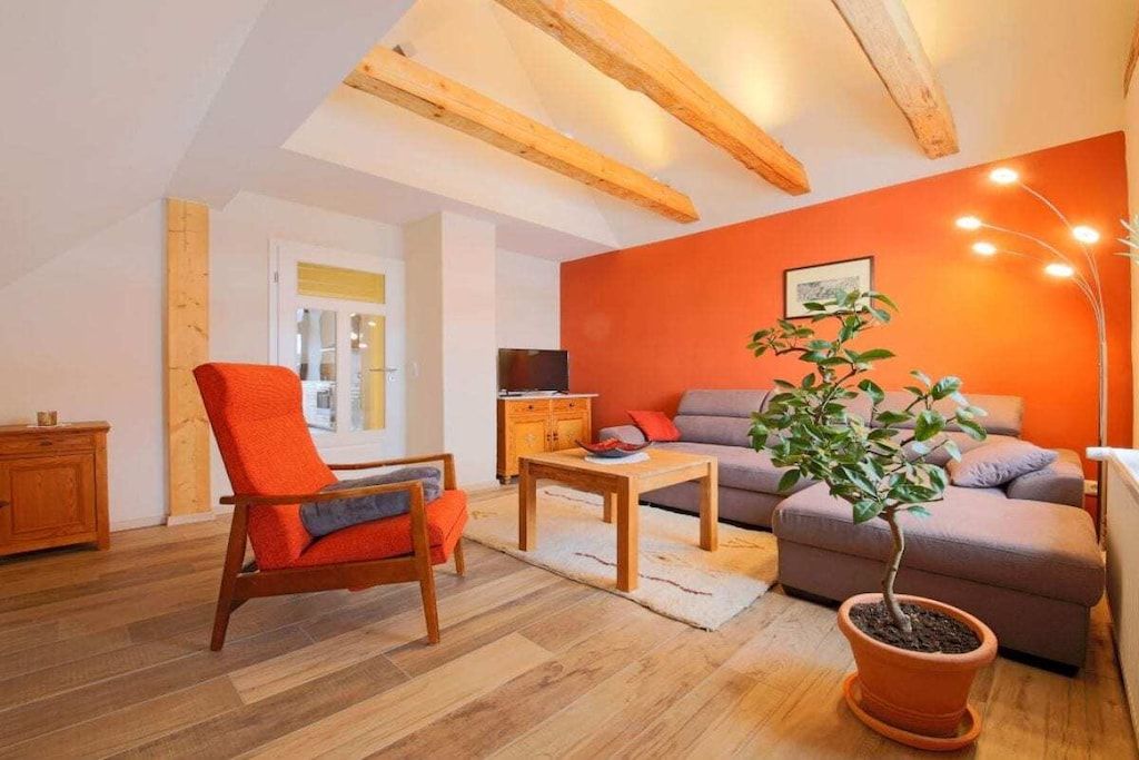 A cozy living room with a wooden chair, sofa, and a potted plant.