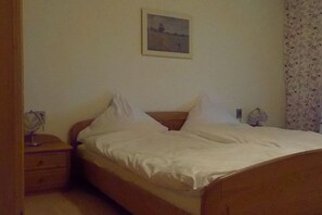 A single bed with white bedding in a room with a plain wall and a floral curtain. - Holiday apartment with 1 bedroom (Konzell)