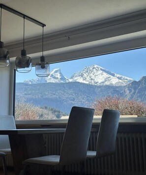 A room with a large window overlooking a mountain range. There are two chairs and a table in the foreground. - Holiday apartment with 1 bedroom (Schönau am Königssee)