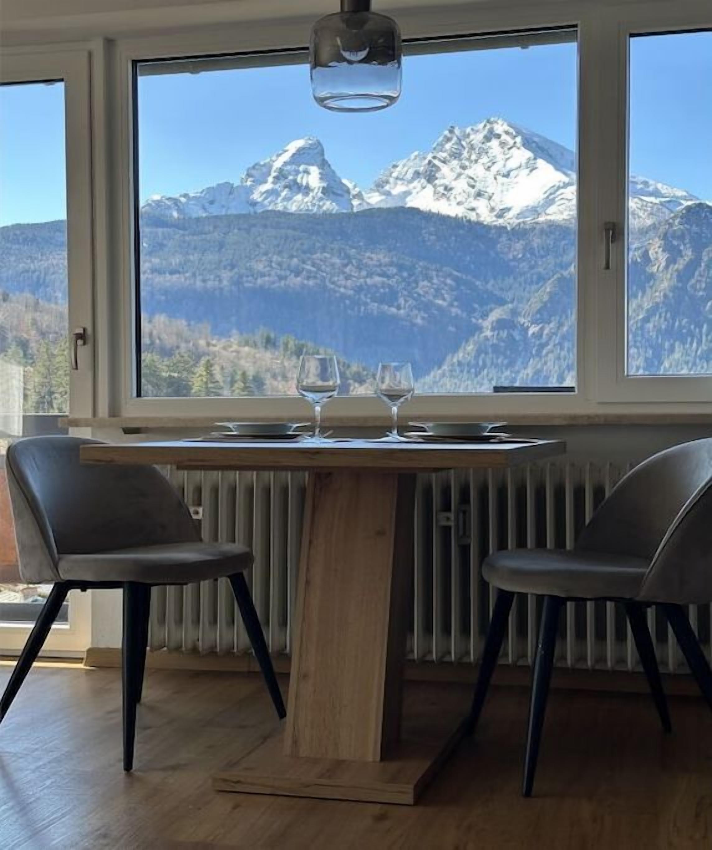 A dining area with a table and two chairs, a window with a mountain view, and a radiator below.