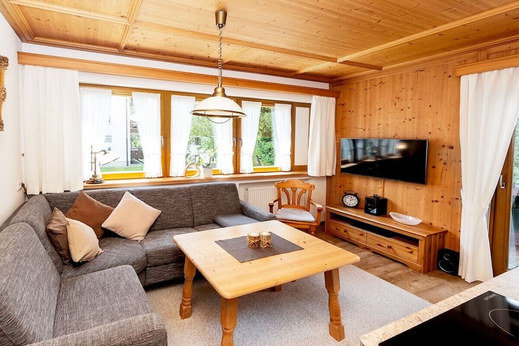 A cozy living room with a sofa, a coffee table, a television, and a wooden ceiling.