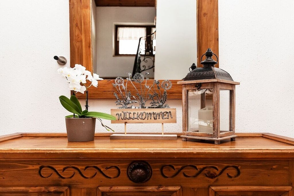 A wooden dresser with a mirror, a potted plant, a welcome sign, and a lantern.
