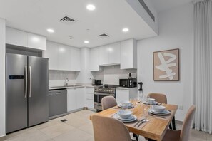 A modern kitchen with stainless steel appliances, white cabinetry, and a dining area set for a meal. - Resort style 2 bedroom by Jumeirah Beach (Dubai)