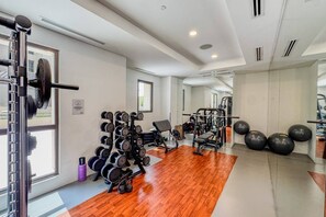 A gym with exercise equipment, a mirror, and a wooden floor. - Resort style 2 bedroom by Jumeirah Beach (Dubai)