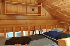 A wooden interior with a bunk bed, a small shelf, and a slanted ceiling. - Wooden house with large garden (Uhldingen-Mühlhofen)