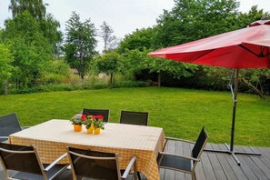 An outdoor dining area with a table set for four, surrounded by chairs, and a red umbrella providing shade. - Wooden house with large garden (Uhldingen-Mühlhofen)