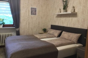 A bedroom with a bed, a nightstand, a window with curtains, a radiator, and a wall-mounted shelf with decorative items. - Holiday apartment with 3 bedrooms (Schiffdorf)