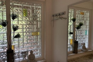 A room with a large window featuring a geometric pattern, a wall-mounted mirror, and a small Buddha statue on the windowsill. - Holiday apartment with 3 bedrooms (Schiffdorf)