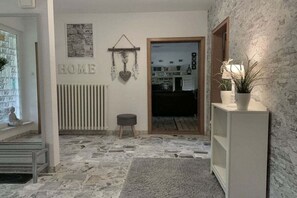 A room with a stone floor, a radiator, a small stool, a shelf with a plant, and a door leading to another room. - Holiday apartment with 3 bedrooms (Schiffdorf)