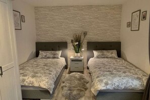 Een slaapkamer met twee bedden, een nachtkastje met een plant en een vloerkleed.