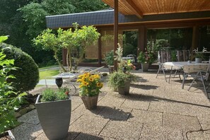 A modern outdoor patio with a dining area, potted plants, and a view of a house. - Holiday apartment with 3 bedrooms (Schiffdorf)