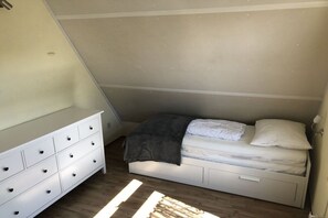 Une petite chambre avec un lit simple, une commode blanche et un plafond en pente.