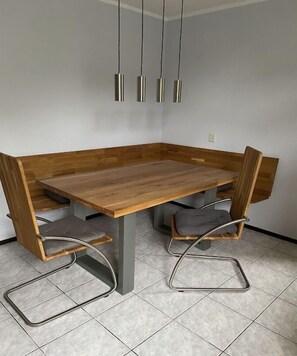 Un espace repas avec une table en bois et des chaises en métal, un luminaire suspendu et un sol carrelé.